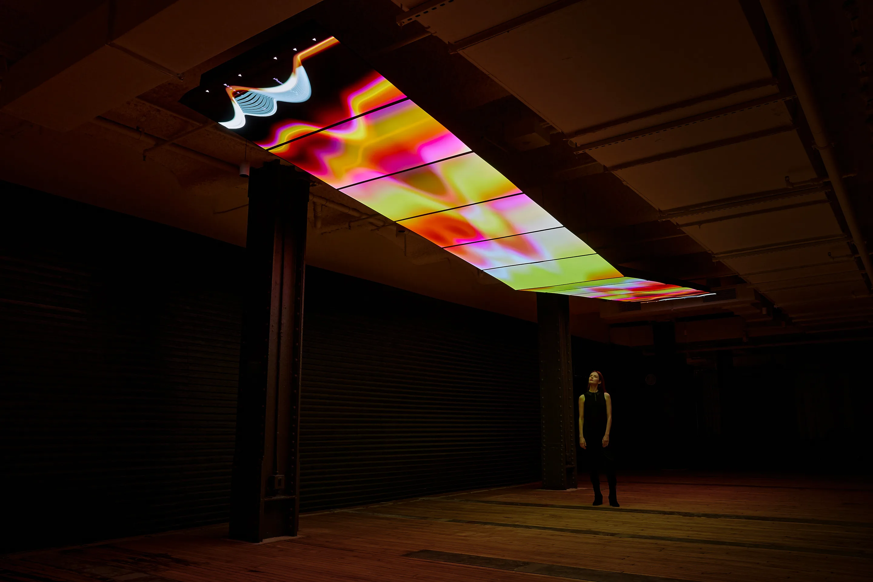 The Skywalk — a suspended screen overhead rendering the day’s accumulated data in colour, with a visitor looking up.