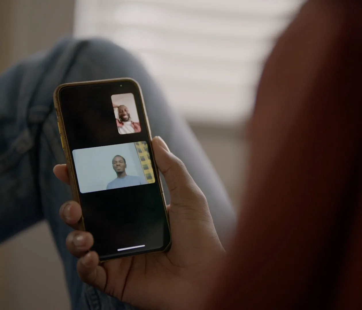 A hand holding a phone running a Messenger video call, two people on screen.