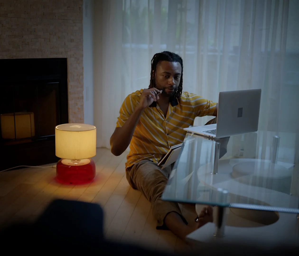 A man at a desk beside a warm lamp and an open laptop, mid-sentence.